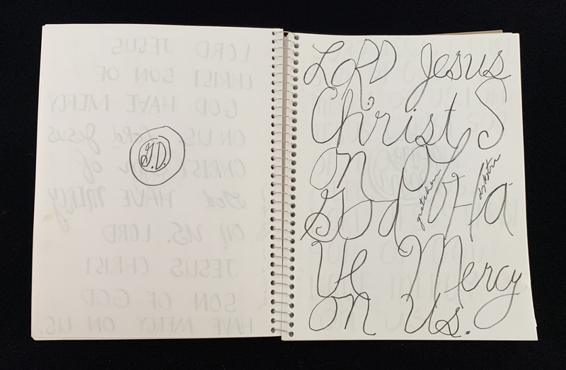 A page from a spiral-bound notebook featuring a calligraphic inscription and faintly visible repeated text in the background.