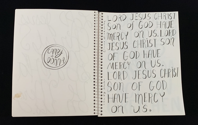A handwritten page with a repeated prayer and a circular logo.