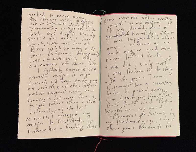 Open notebook with handwritten text on cream-colored pages, photographed against a black background.