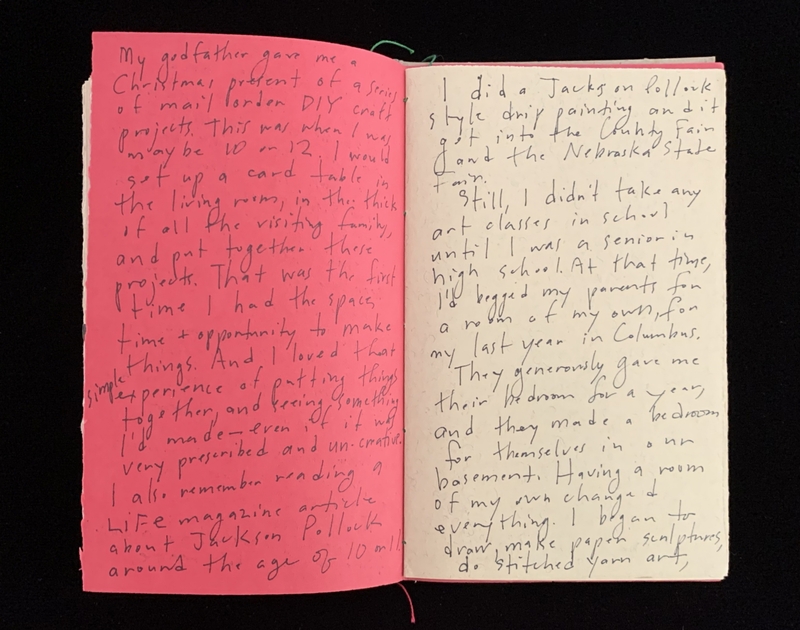 An open notebook with handwritten text on pink and off-white pages.