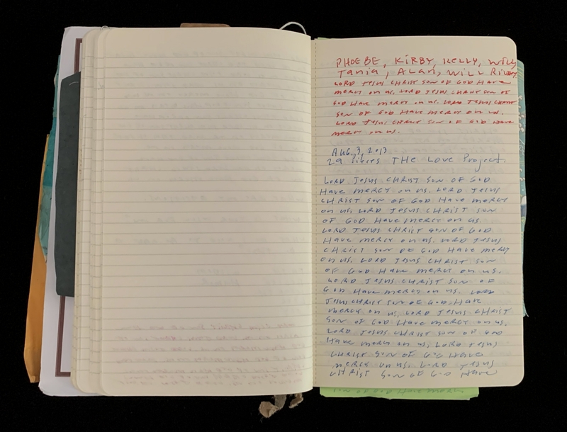 An open notebook with handwritten text in blue and red ink, resting against a black background.