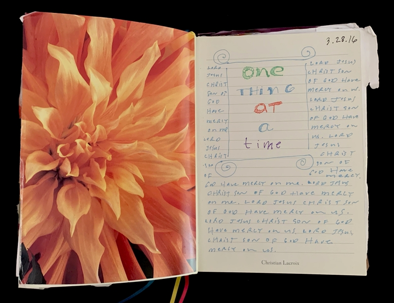 An open journal with a vivid orange flower on the left page and handwritten text with colorful letters on the right.