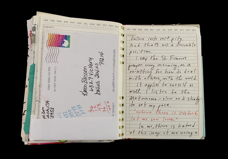 : A handwritten note in a spiral-bound notebook with a postcard and a calendar page.