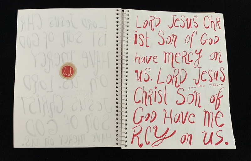 A handwritten page with religious phrases and a circular sticker.