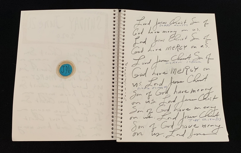 A handwritten page with a circular sticker and repeated script prayers.