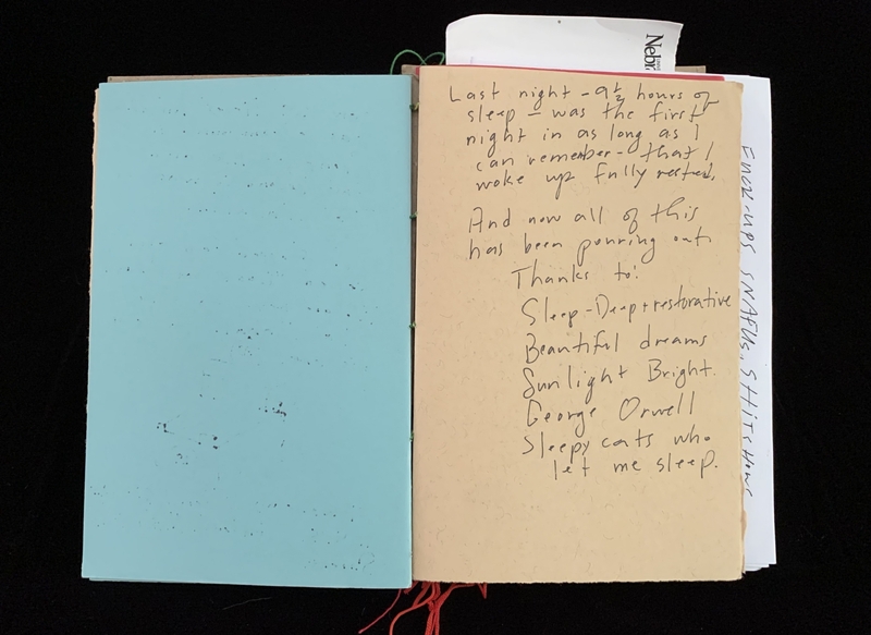 An open notebook with a blank blue page on the left and handwritten text on a beige page on the right.