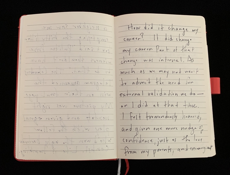 Open notebook with handwritten text on lined pages, red bookmark on the right.