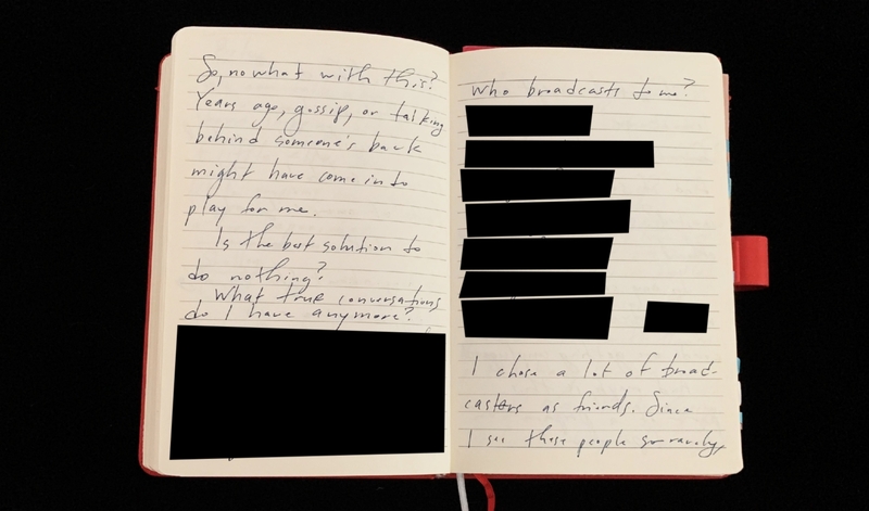 An open notebook with redacted handwritten text and a red cover.