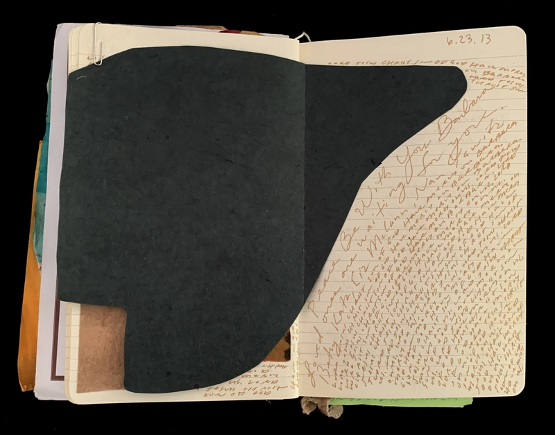 Open notebook with a dark paper insert, covered in dense cursive writing.