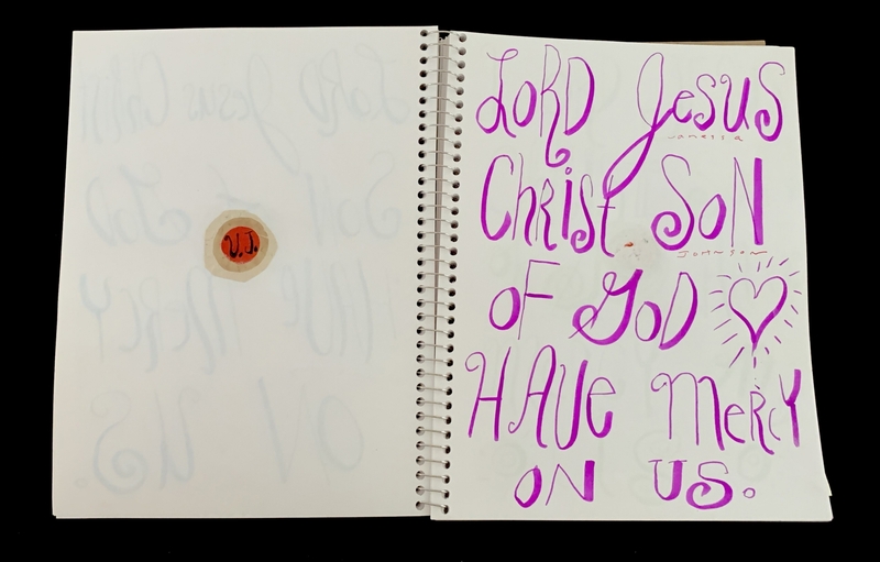 A handwritten prayer page featuring a religious phrase and a small circular sticker.