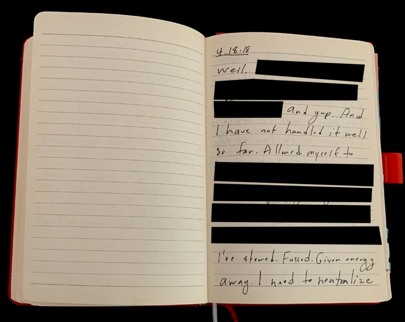 An open notebook with one blank page and one page with redacted handwritten text.