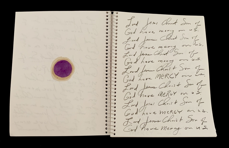 A handwritten page with repeated prayers and a circular purple object on the left side.