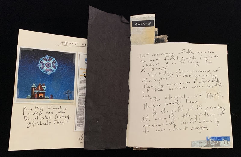 Open scrapbook with artwork and handwritten notes, partially obscured by black paper.