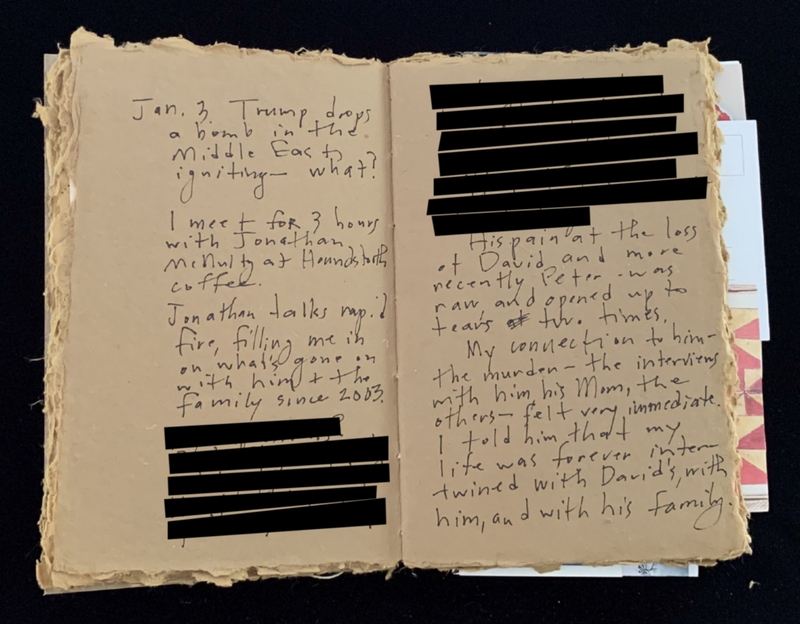 An open notebook with handwritten notes and black redactions on one page.