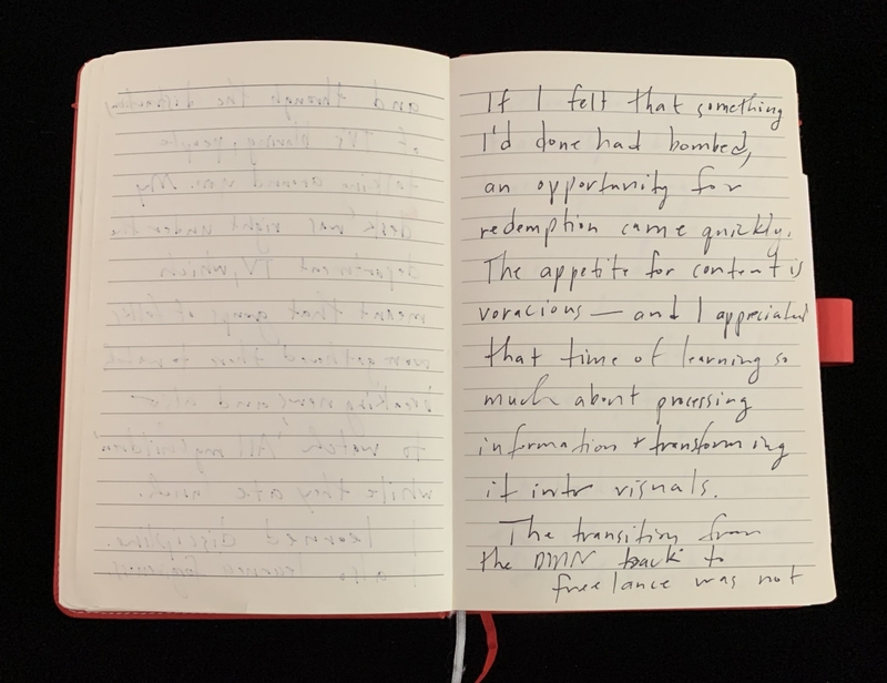 An open notebook with a red cover and handwritten text on the pages. The right page has clear writing.