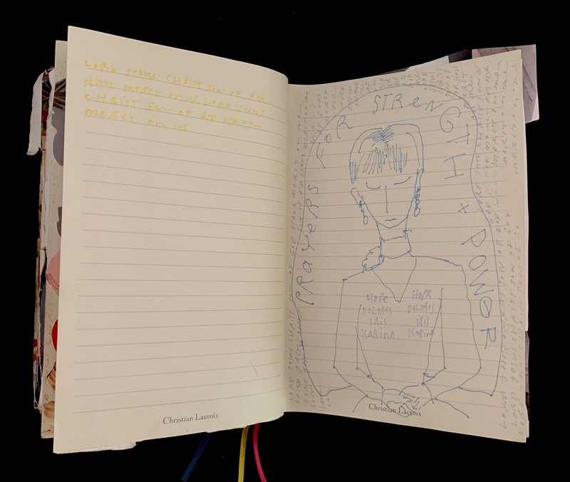 An open journal with handwritten text and a blue ink drawing of a person encircled by the words "Prayers for Strength + Power."