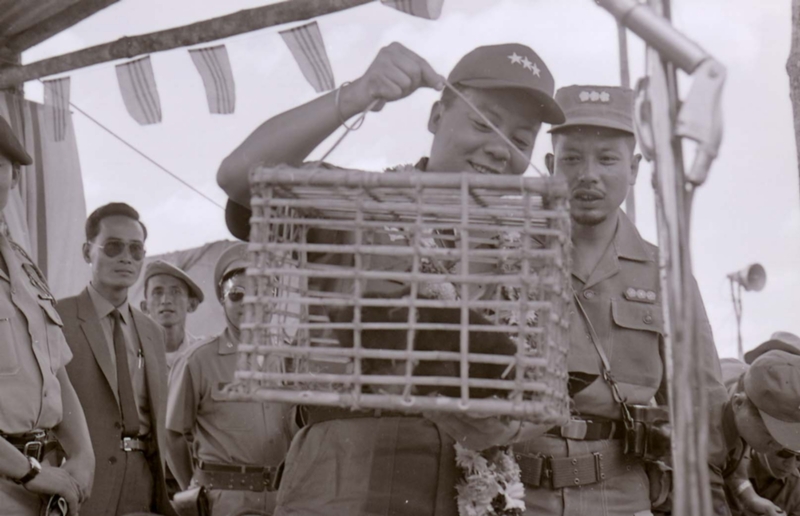 Nguyá»…n KhÃ¡nh appears to be holding some kind of animal in a small cage, possibly a monkey. Others look on the background.