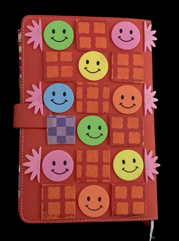 Red notebook cover with colorful foam smiley faces and squares in a grid pattern.