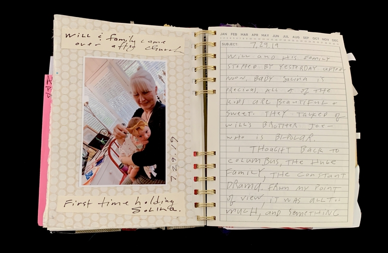A handwritten journal entry with a photograph of a woman holding a baby, accompanied by notes about a family visit.