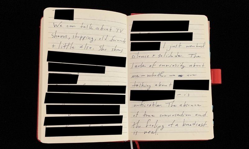 An open notebook with redacted handwritten text covered by black bars.