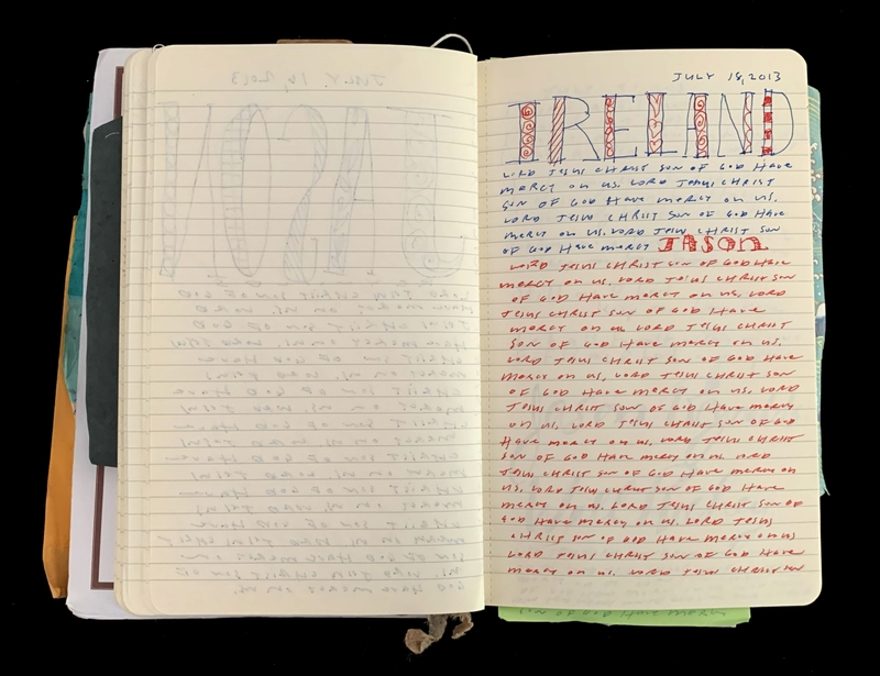 An open notebook with decorated lettering and handwritten text in pencil and ink filling the pages.