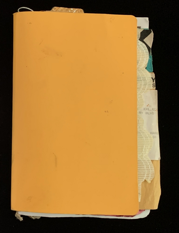 A closed orange notebook with papers sticking out against a black background.