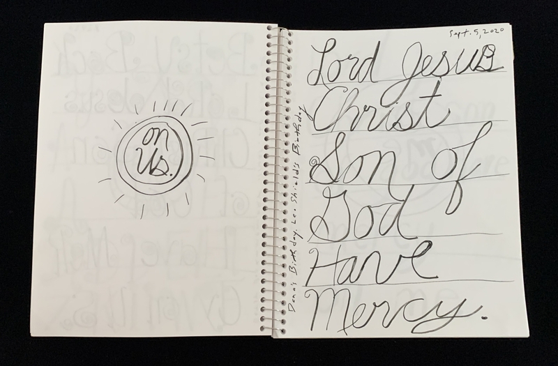 A handwritten page in a spiral notebook with a simple doodle and a prayer written in cursive.