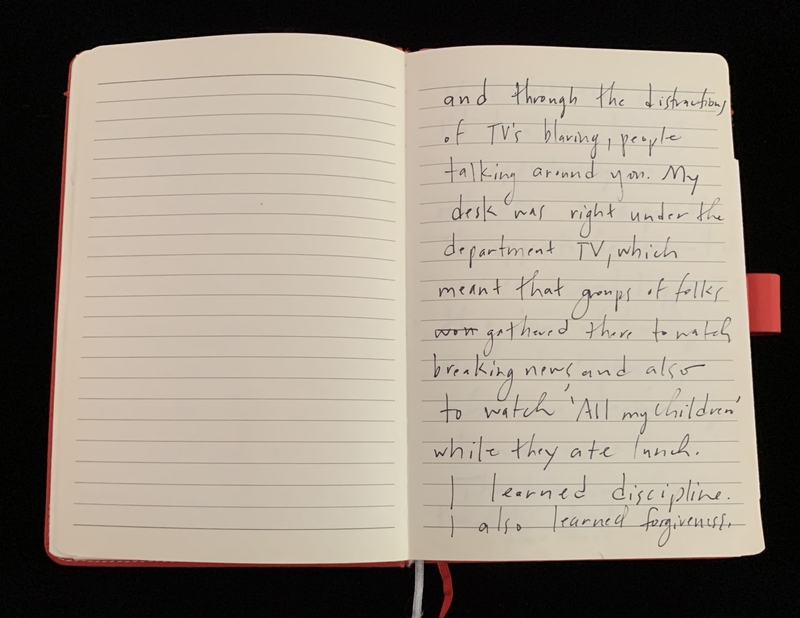 Open notebook with one lined page full of handwritten text and another blank page, with a red cover partially visible.
