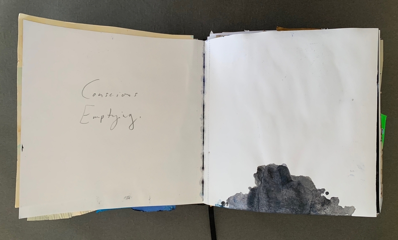 A journal page with the words "Conscious Emptying" written on the left page and a dark, abstract watercolor splash on the right page.