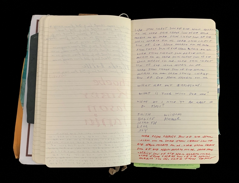 An open notebook with handwritten text and additional papers underneath.