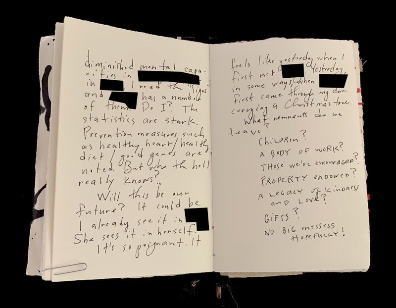 Open notebook with handwritten text and redacted sections.
