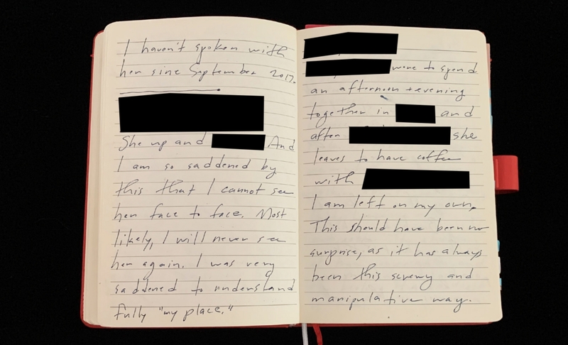 An open notebook with handwritten text and redactions on both pages.