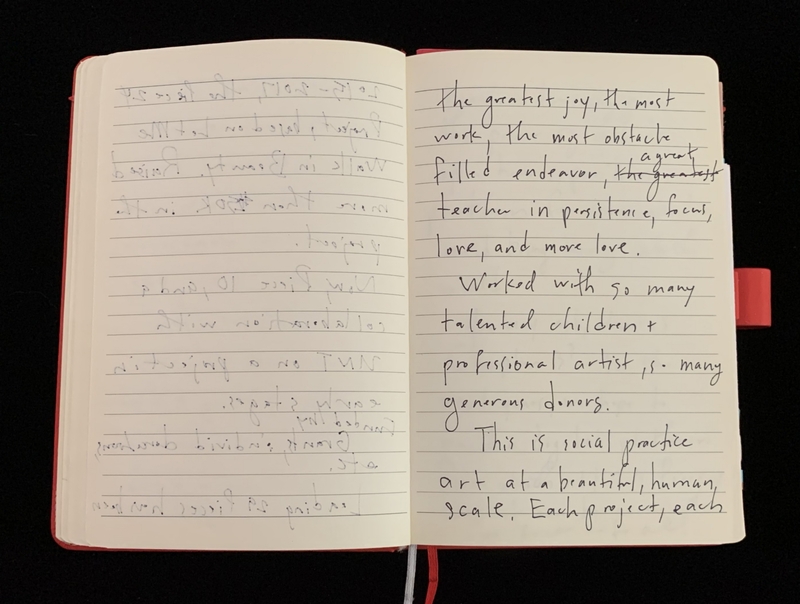 An open notebook with handwritten text on lined pages against a black background.