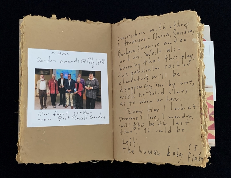 An open notebook with a photograph and handwritten text on aged, textured pages.