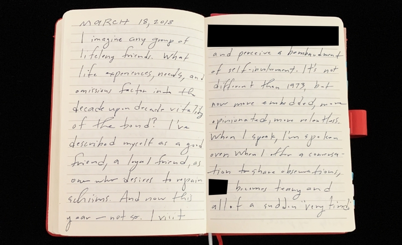 Open notebook with handwritten text, partially redacted with black rectangles.