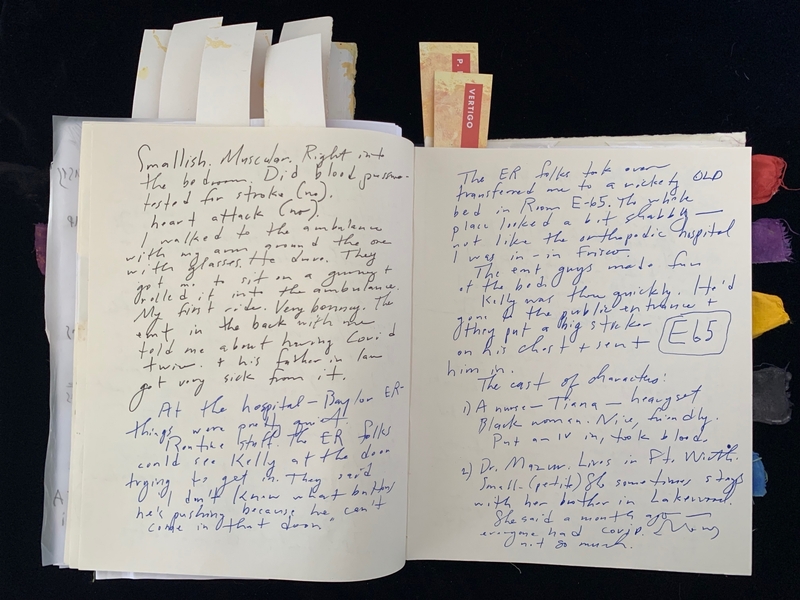 An open journal with handwritten text in black and blue ink, and colored tabs on the page edges.
