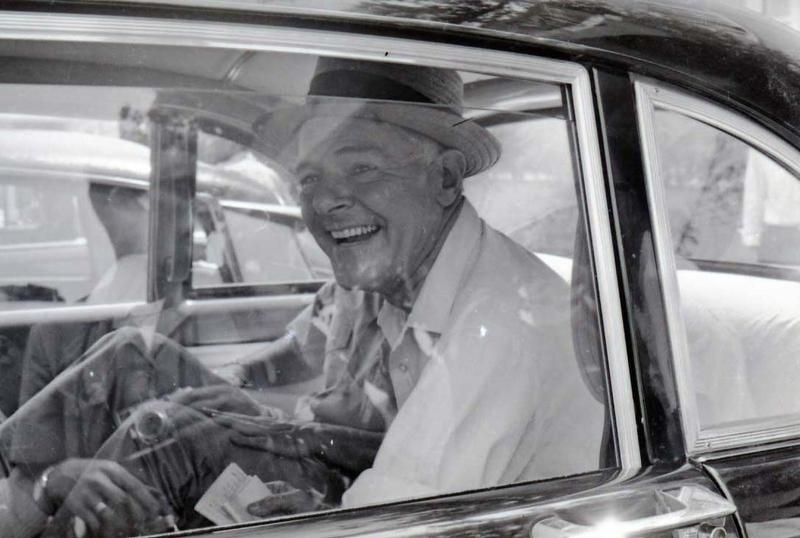 Henry Cabot Lodge Jr wearing a hat is seated inside of a vehicle. He smiles at the camera.