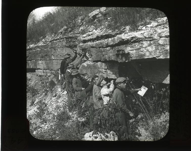Original caption:  Ledge formerly quarried at Green's exposure in lower part of bluffs opp. So. Bend. NAB. Oct 21, 1911 Group of men viewing and stand beneath ledge. Cass County. (121111-00246)