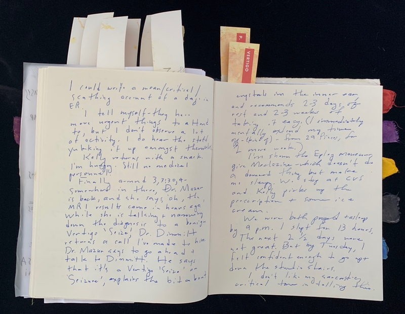 Open journal with blue handwritten text on both pages, colorful fabric swatches visible on the right.