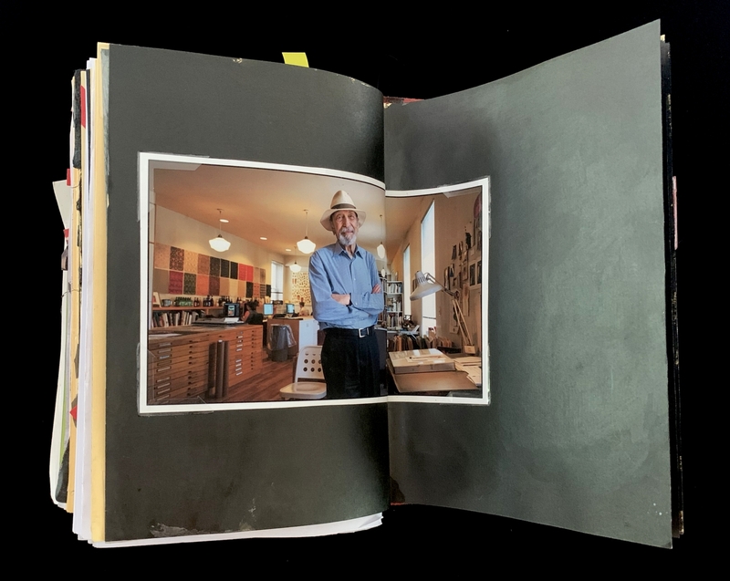 A photograph of a man in a blue shirt and hat stands in a well-lit, organized workspace with various items and furniture.