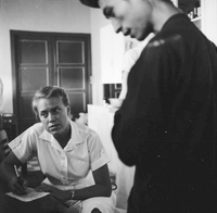 An American nurse speaking to someone out of the photograph. She writes notes on their conversation.