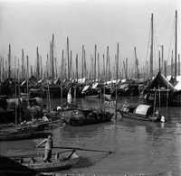 "Macau" A young boy is standing in a boat in the foreground, other boats are in the water surrounding him in the background.