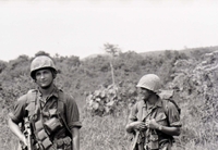 Two American soldiers are standing in a field smiling.