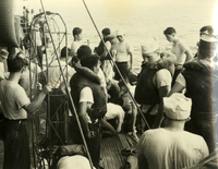 "First Aid to Injured - Immediate first aide is given to one of the injured crewmen aboard USS Oriskany in the vicinity of the ship's quarterdeck. The fire which blazed on the aircraft carrier for three hours on Oct. 26, took 43 lives and injured 16." A large group of American men stand on the deck of a ship. A few wear life jackets.
