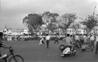 "Unidentified", Photo of a protest. A large crowd of Vietnamese people walk in a major intersection with banners. Men riding bikes and motorcycles have stopped to watch in the foreground.