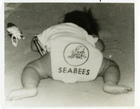 "Kelly Faith, Daughter of Navy SEABEE Equipment Operator Third Class and Mrs. Robert G. Hammond, just joined the Seabee Ranks and announced her arrival with the Seabee emblem decorating her 'uniform of the day.' Poppa hasn't seen the new lady yet. He's a member of Mobile construction Battalion 133 and has been in Vietnam since Feb. He's anxiously awaiting his return to homeport at the Gulfport (Mississippi) Seabee Center and a 'get acquainted' leave period."  Baby wearing Seabee clothing. Seabees news release 93-67 (51).