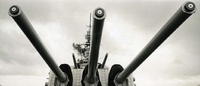 "The guns of the USS Newport News, are the most rapid fire 8 inch guns in the navy. The Newport news and other cruisers play a vital part in the Navy's operation Sea Dragon off the coast of the North Vietnam." Three cannon or gun barrels on a naval ship face the camera. The top of the ship is in the background.