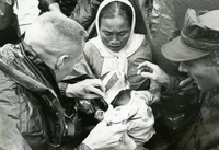 "Better than bullets - Navy Doctor Jerry A. Shields dresses a Vietnamese child's head after treating her for an abscess. Her mother looks on, surrounded by Marines. The 'clinic' is an amphibious tractor from the 1st Amphibian Bn., 3rd Marine Division. Twice a week amtracs visit a sampan community on the Han River at Da Nang to take medical help to the people, most of whom have never before received any medical treatment. Says a veteran Marine: 'This sure beats bullets as a way to win, and it's so much more lasting.'" A Vietnamese woman holds a baby who has a bandaged head. Two American men, one smoking a cigar, check the bandages.