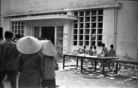 "Students wrecking min. of info." A crowd of people filing into a building. To the right of the door, five children park their bikes near a table.