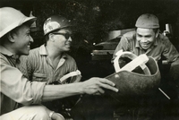 "'Take Five' - Mr. Melvin Werner (center), a welder with the U.S. Naval Shipyard, Pearl Harbor, Hawaii, and two Vietnamese welders with the Saigon Naval Shipyard relax for a few minutes between periods of instructions on better welding techniques. Mr. Werner and three other welders from the Naval Shipyard at Pearl Harbor, currently on a six weeks tour under the United States Military Assistance Program, are teaching welding techniques to Vietnamese welders at the Saigon Naval Shipyard. They will return to Pearl Harbor on 12 December." An American man and two Vietnamese men laugh together. They are holding welding masks.